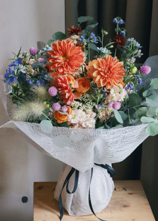 Vibrant bouquet with orange dahlias, purple thistles, and mixed greenery