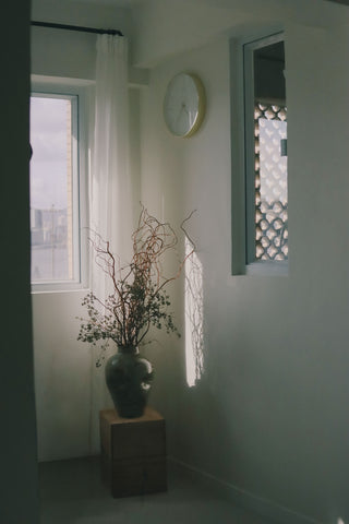 Sunlit corner with a vase of curly branches on a wooden stand