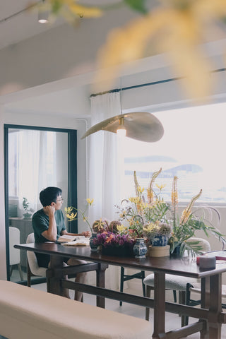 Person sitting at a table with floral arrangements in a well-lit room