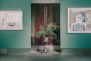 Art gallery entrance with two framed artworks and a flower arrangement.